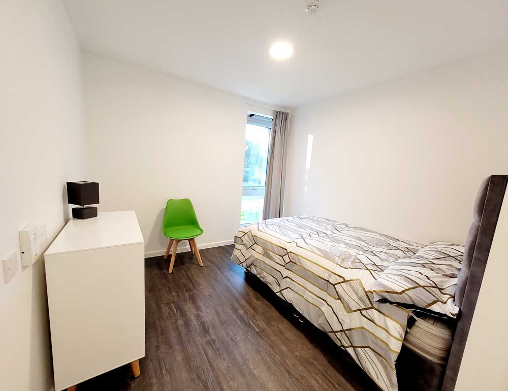 Modern, small white bedroom with bed, chair and chest of drawers at YMCA City Gateway Accommodation