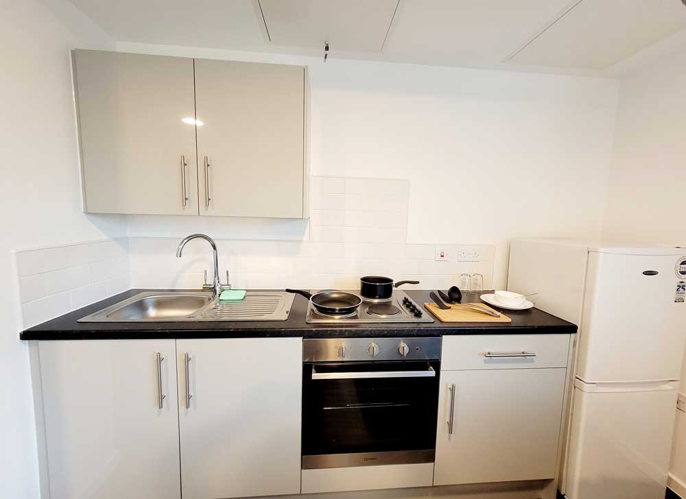White kitchen with hob, oven and fridge at YMCA City Gateway Accommodation