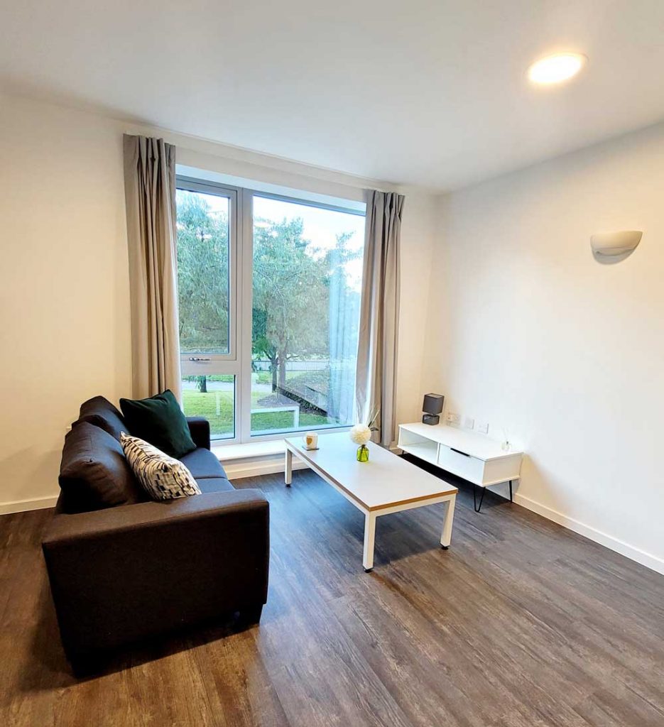 Small white room with a sofa, coffee table and media unit in YMCA City Gateway accommodation