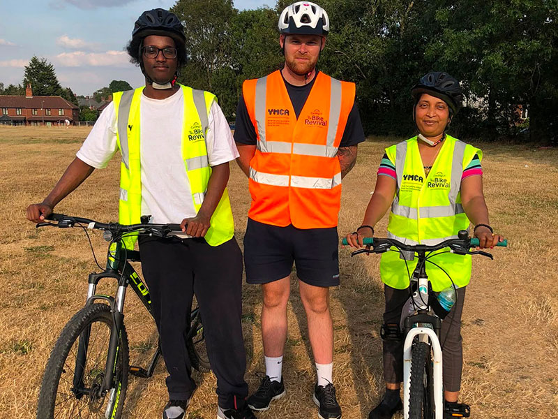 YMCA Staff member stood with two new cyclists in high vis vests over at Sandwell Valley to boost their confidence in cycling.
