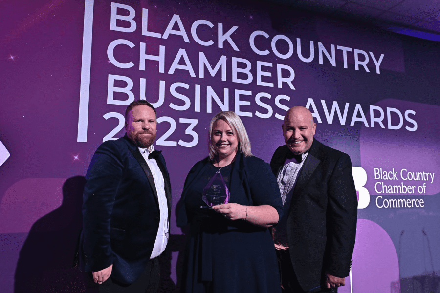 Kellie Simcox smiling to camera holding her award, stood with two men who were sponsoring the event.