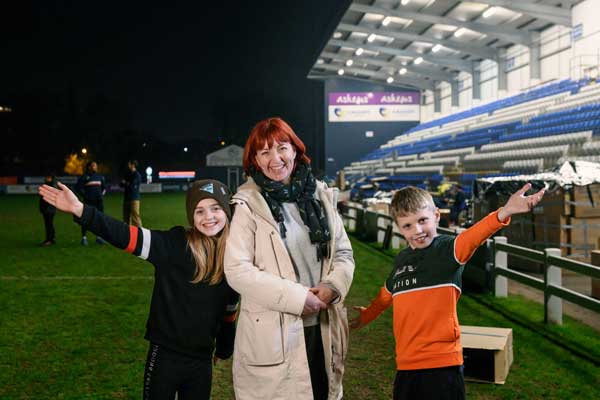 Mother and children standing on a football pitch in front of cardboard boxes, smiling and taking part in YMCA Sleep Easy event