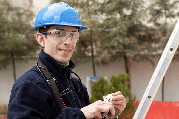 Young man in hard hat and safety goggles working on electrics outside.