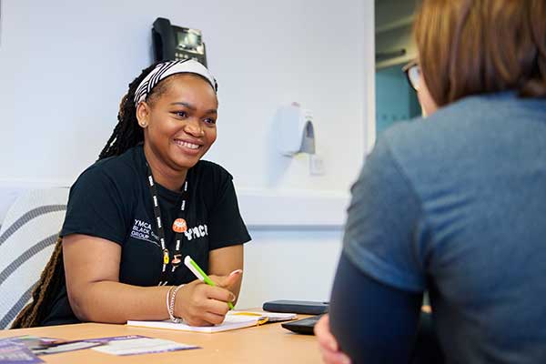 Young smiling woman working for YMCA, speaks to a young person across the desk from her.