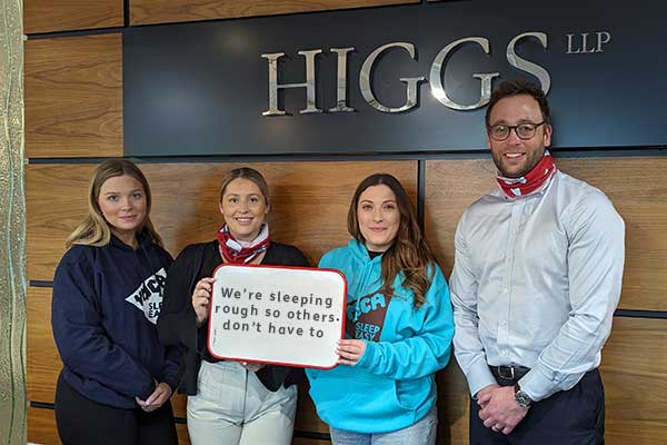 4 members of Higgs LLP team smiling to camera wearing Sleep Easy hoodies holding a sign that reads 