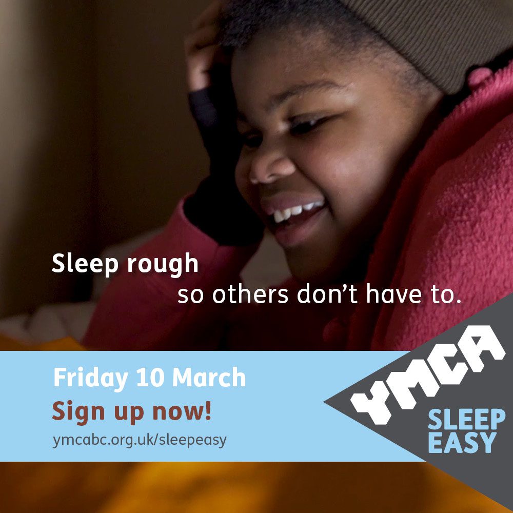 Young girl lying in cardboard box wearing a beanie hat and gloves laughing with a friend at YMCA Sleep Easy