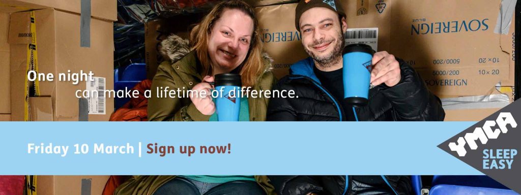 Two people sat inside a fort of cardboard boxes holding branded thermos flasks to promote YMCA Sleep Easy fundraising event