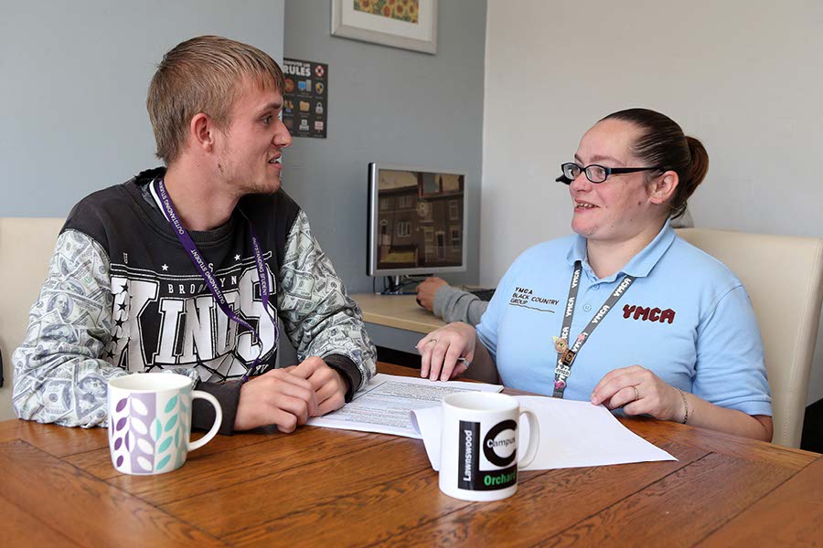 Young man and female YMCA housing employee sat at a table working through some tenancy paperwork.
